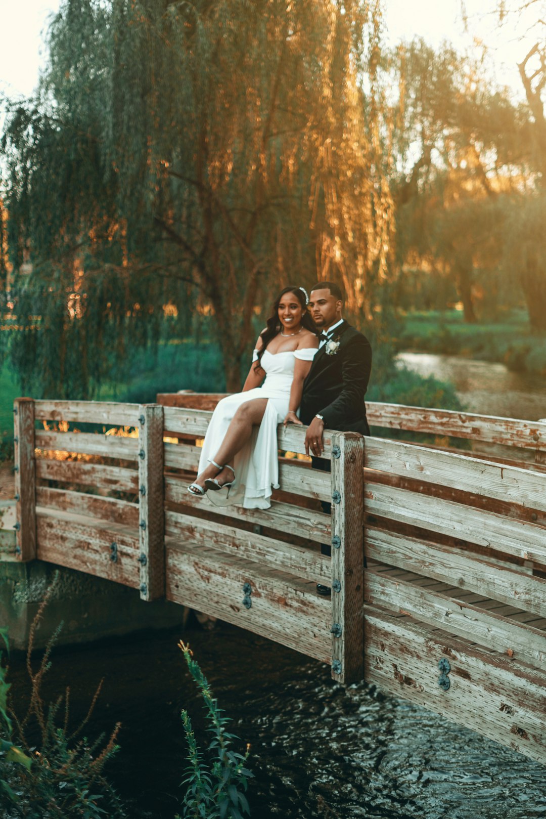 couple sitting on wooden bridge over river during daytime