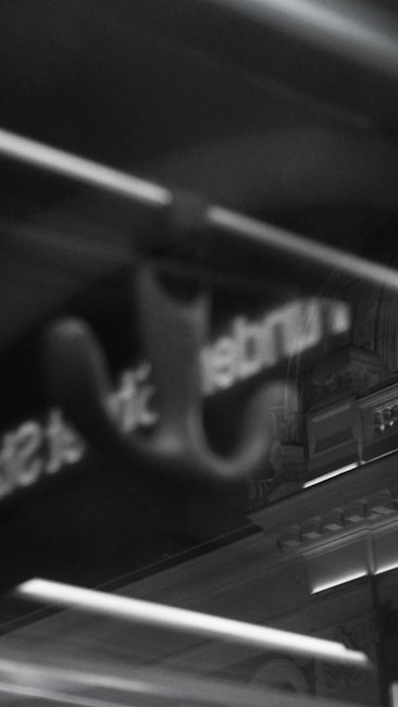 A dimly lit, monochrome image with blurred text in the foreground and architectural details in the background. The reflection of a structure, possibly a building with ornate designs, is visible.