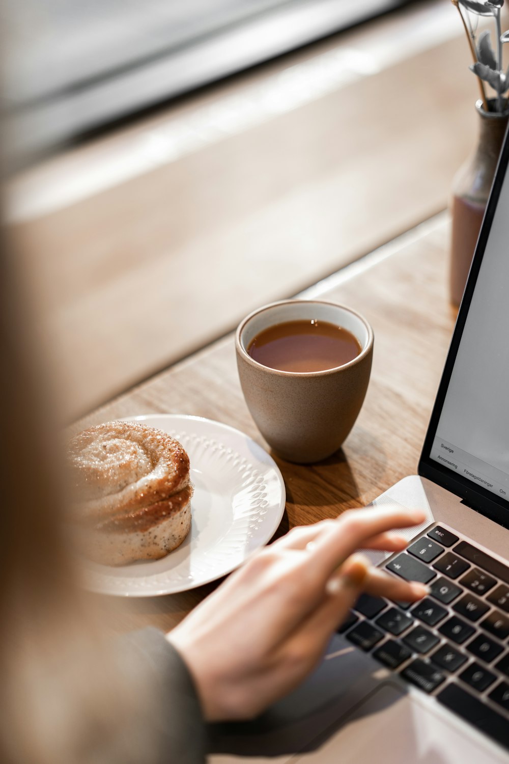 person using macbook pro beside white ceramic mug with brown liquid