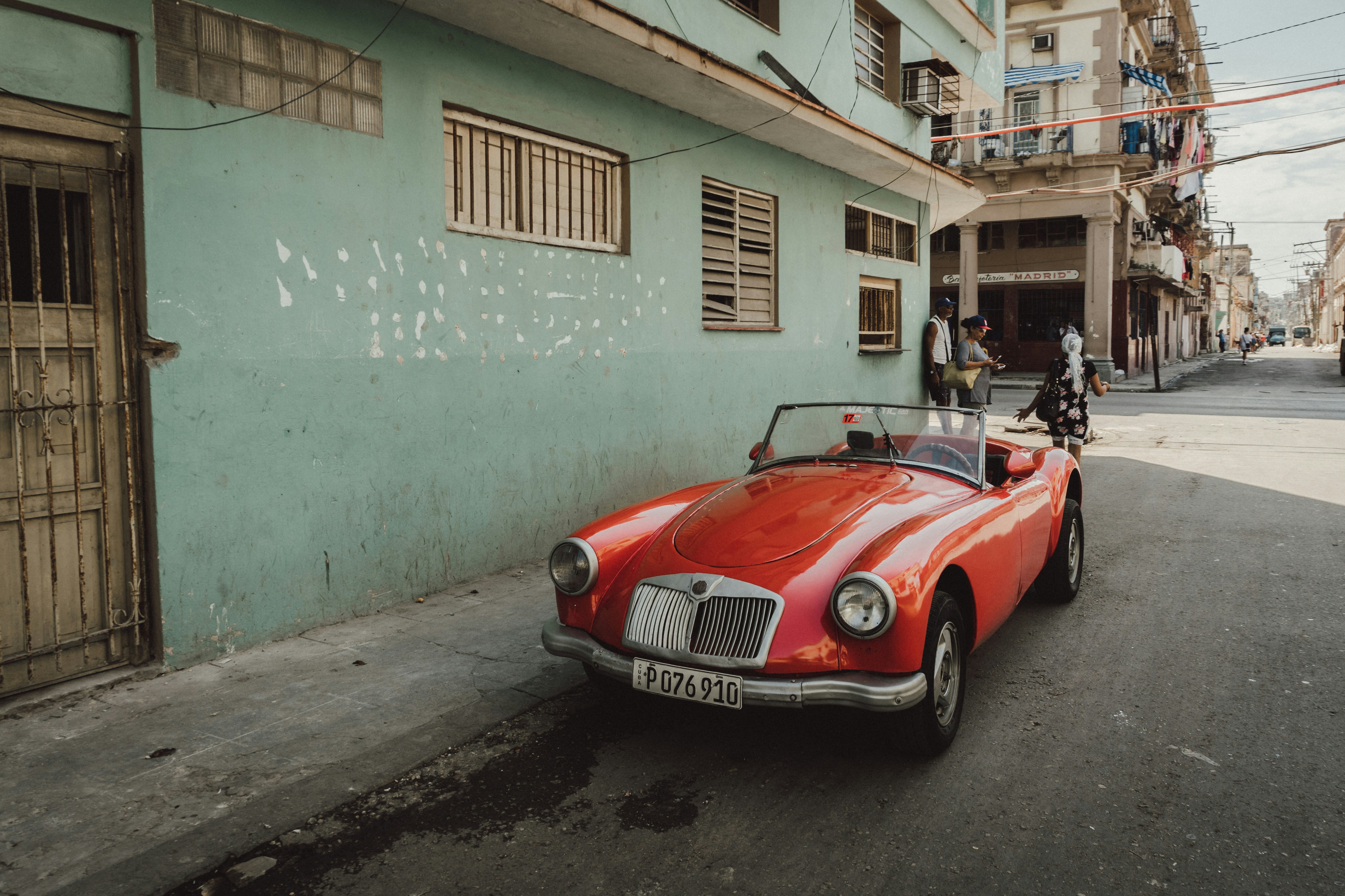 red convertible car parked beside white and green concrete building during daytime