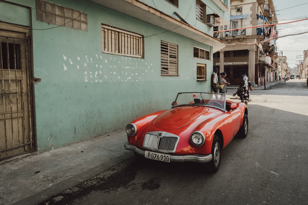 red convertible car parked beside white and green concrete building during daytime