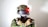A person wearing camouflage military gear and VR headset, with crossed arms holding controllers. The helmet is equipped with a headset and a glowing red light.