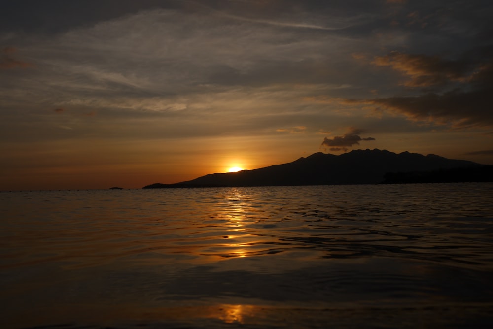 silhouette of mountain near body of water during sunset