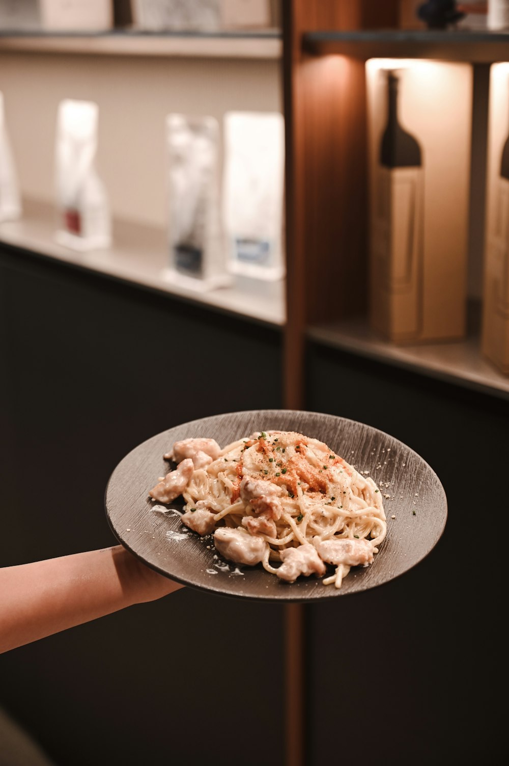 person holding black ceramic plate with pasta dish