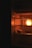 A dimly lit refrigerator with a glowing light on the inside. On a shelf, there is a piece of bread or food item partially unwrapped, with some greens next to it. The overall atmosphere is dark with warmth emanating from the light bulb inside.