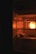A dimly lit refrigerator with a glowing light on the inside. On a shelf, there is a piece of bread or food item partially unwrapped, with some greens next to it. The overall atmosphere is dark with warmth emanating from the light bulb inside.