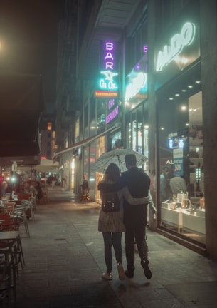 A cozy couple holding hands under violet-hued city lights at dusk.