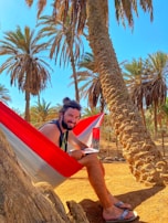 A hammock strung between palm trees with a tablet resting on it under clear blue skies.