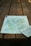 A detailed map is spread out on a wooden picnic table, capturing a rustic and natural setting. The map appears to depict a geographical area with terrain features and possibly hiking trails.