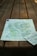 A detailed map is spread out on a wooden picnic table, capturing a rustic and natural setting. The map appears to depict a geographical area with terrain features and possibly hiking trails.