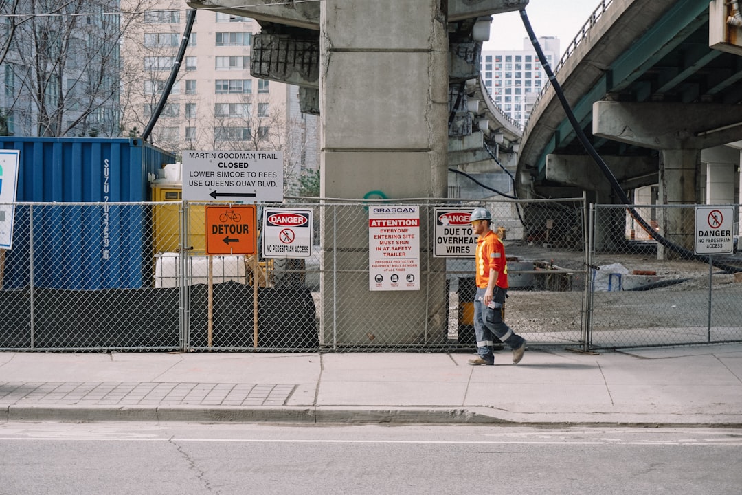 man in orange jacket standing on sidewalk during daytime