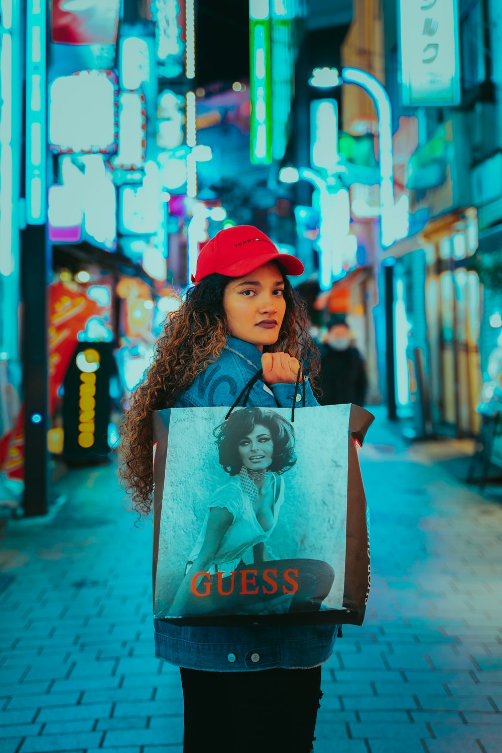 a woman holding a guess shopping bag on a city street
