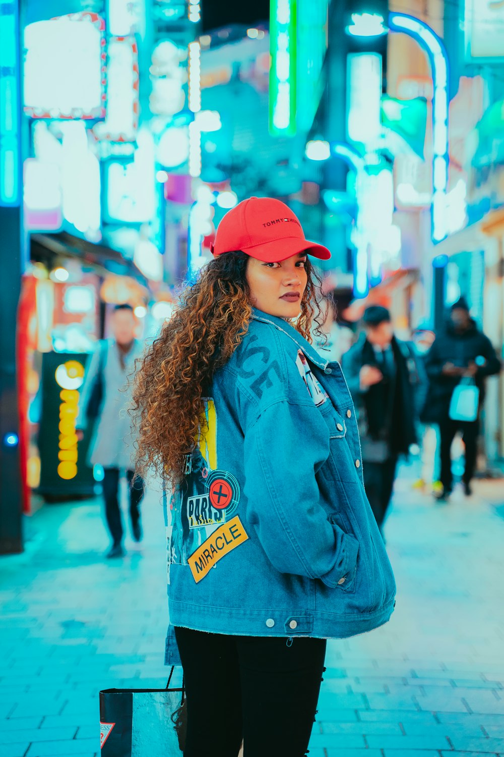 woman in blue denim jacket and red knit cap standing on street during daytime