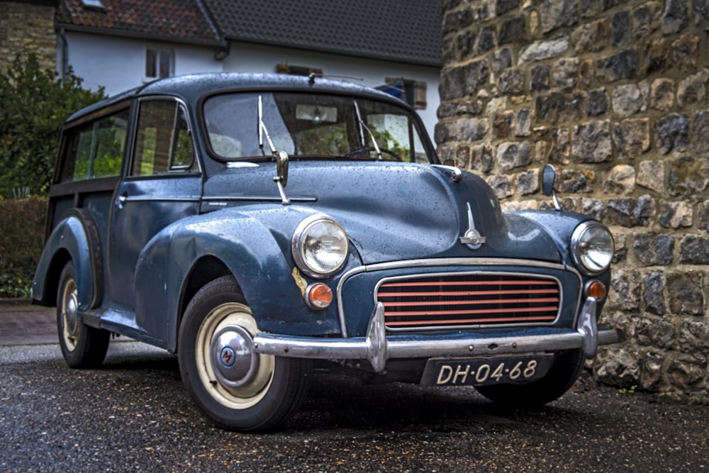 blue classic car parked beside brick wall