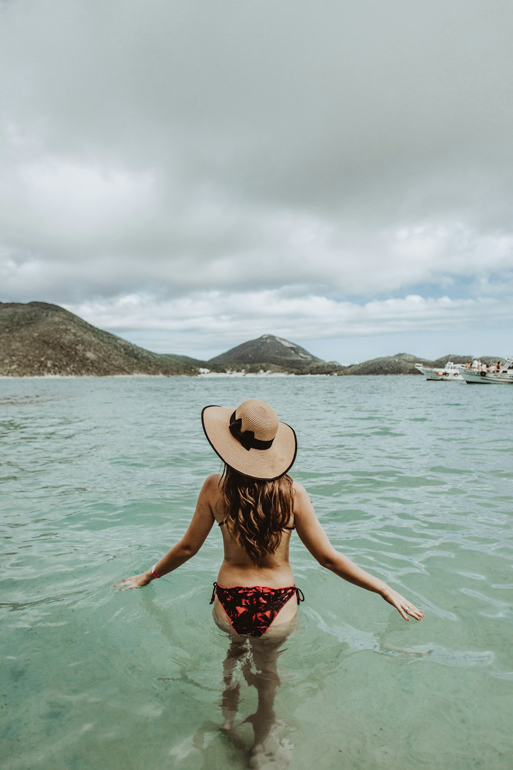 woman in red and white floral bikini wearing brown sun hat standing on sea water during