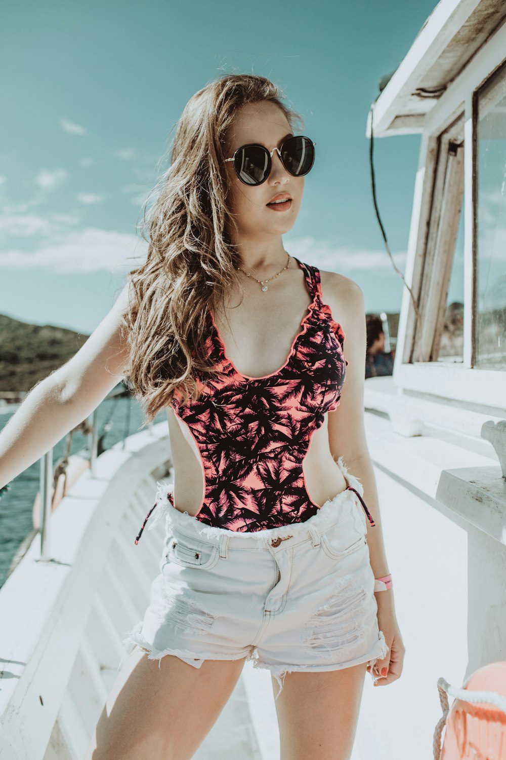 woman in red and white floral tank top and white denim shorts wearing black sunglasses