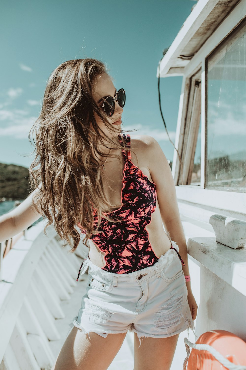 woman in red and white floral tank top and white denim shorts wearing black sunglasses