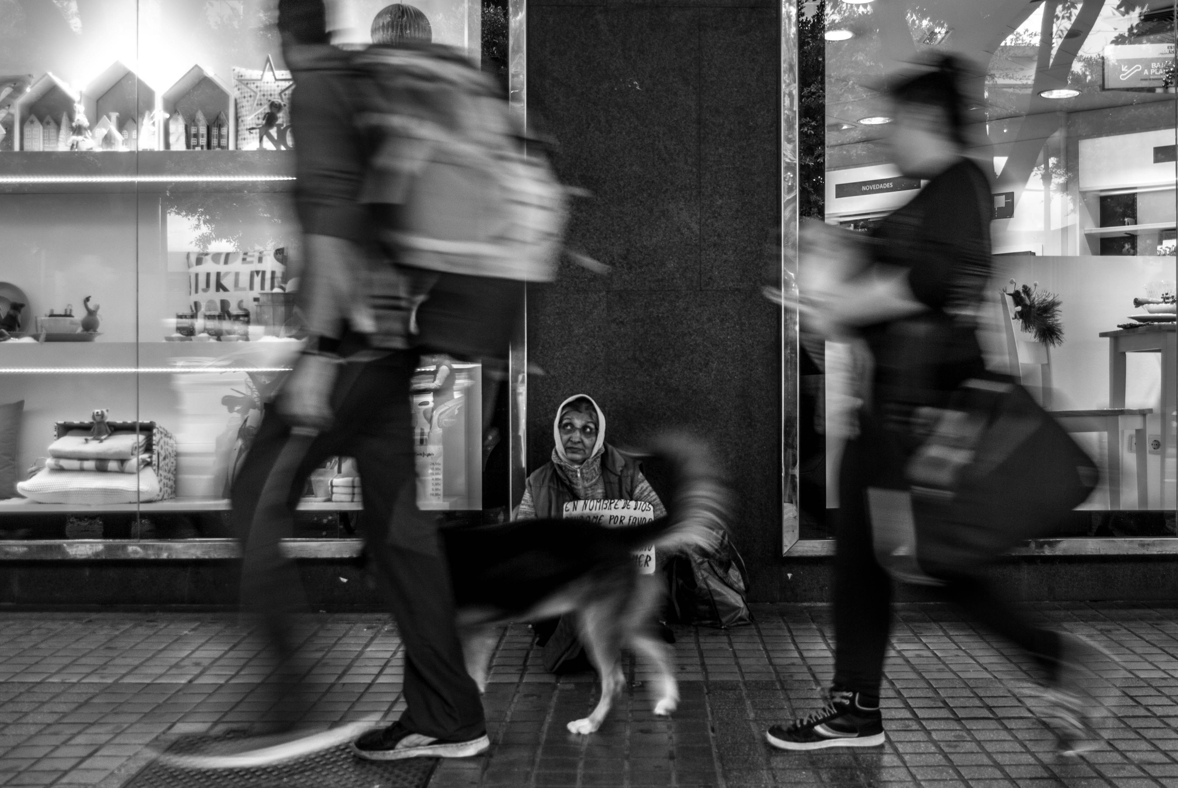 Aprender a mirar a nuestro alrededor es la máxima de esta toma. El emplazamiento y el entorno hacen de esta fotografía una curiosa instantánea. Un centro comercial, una calle abarrotada, la miseria y el capitalismo en su máximo explendor.