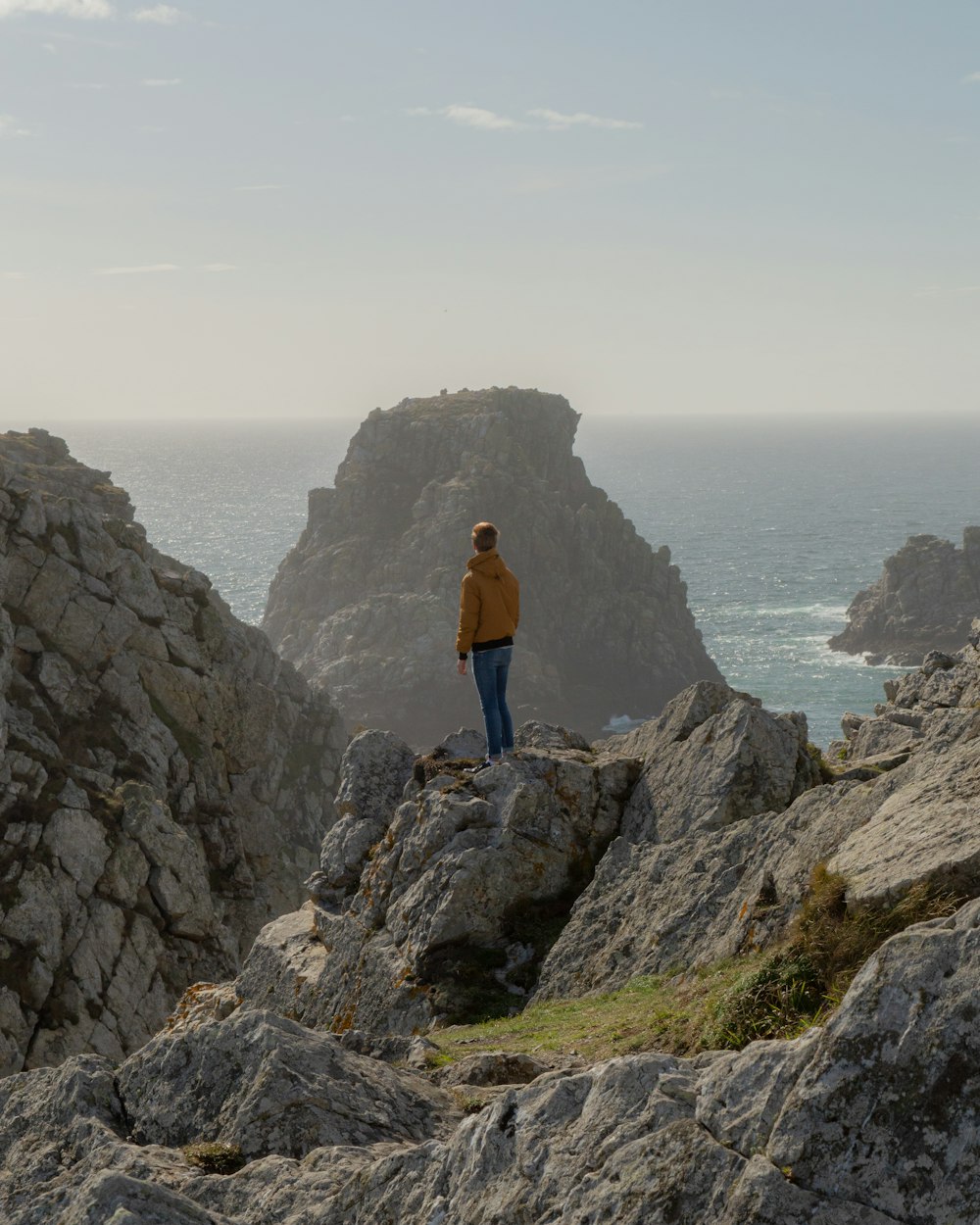 person in blue jacket standing on rock formation near body of water during daytime