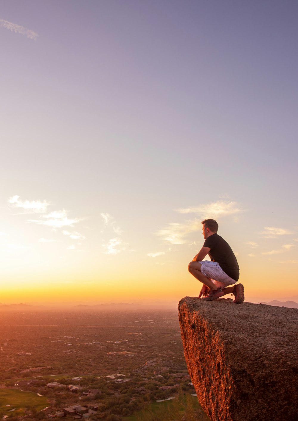 woman in black tank top sitting on brown rock formation during sunset