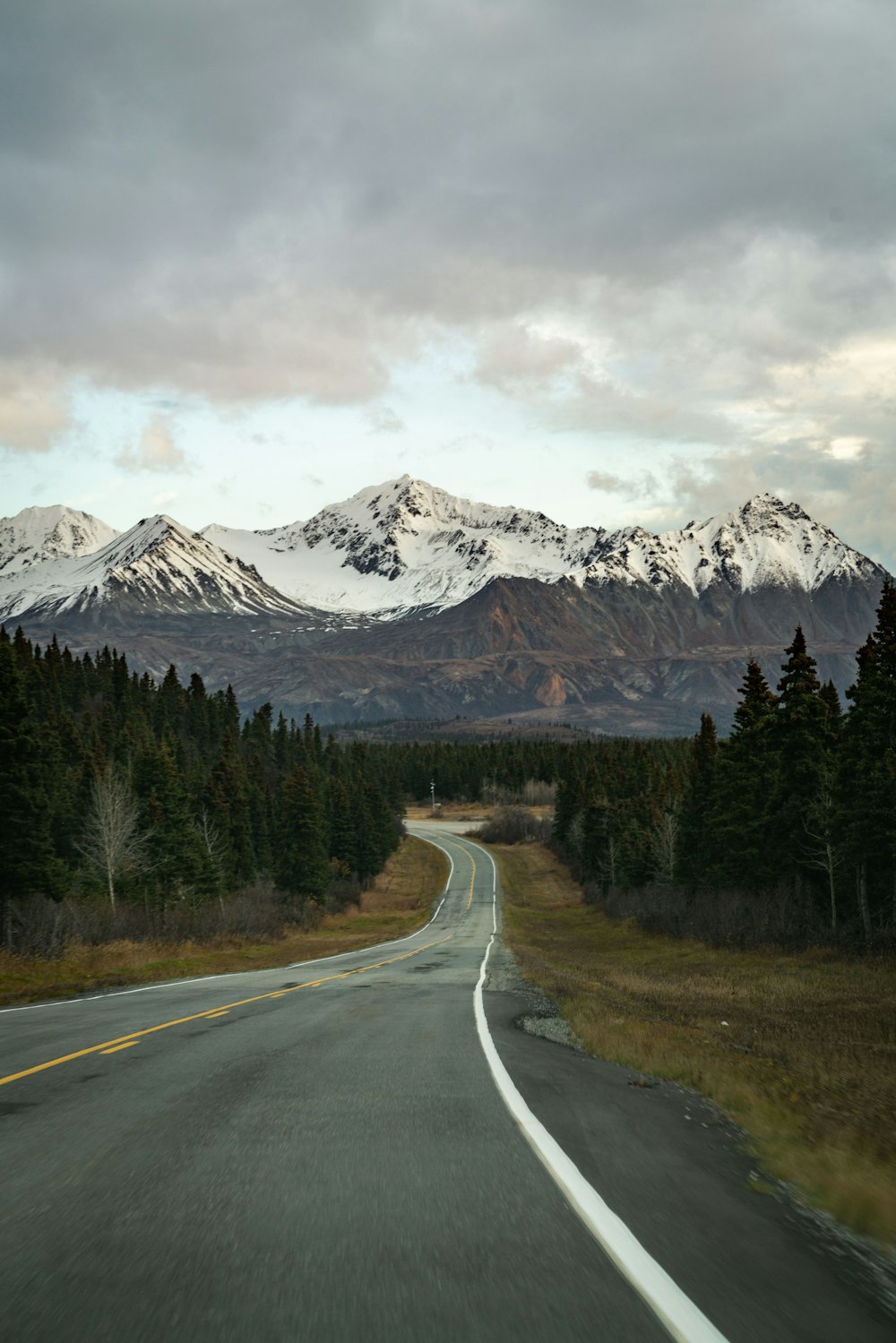 gray concrete road near green trees and snow covered mountain during daytime