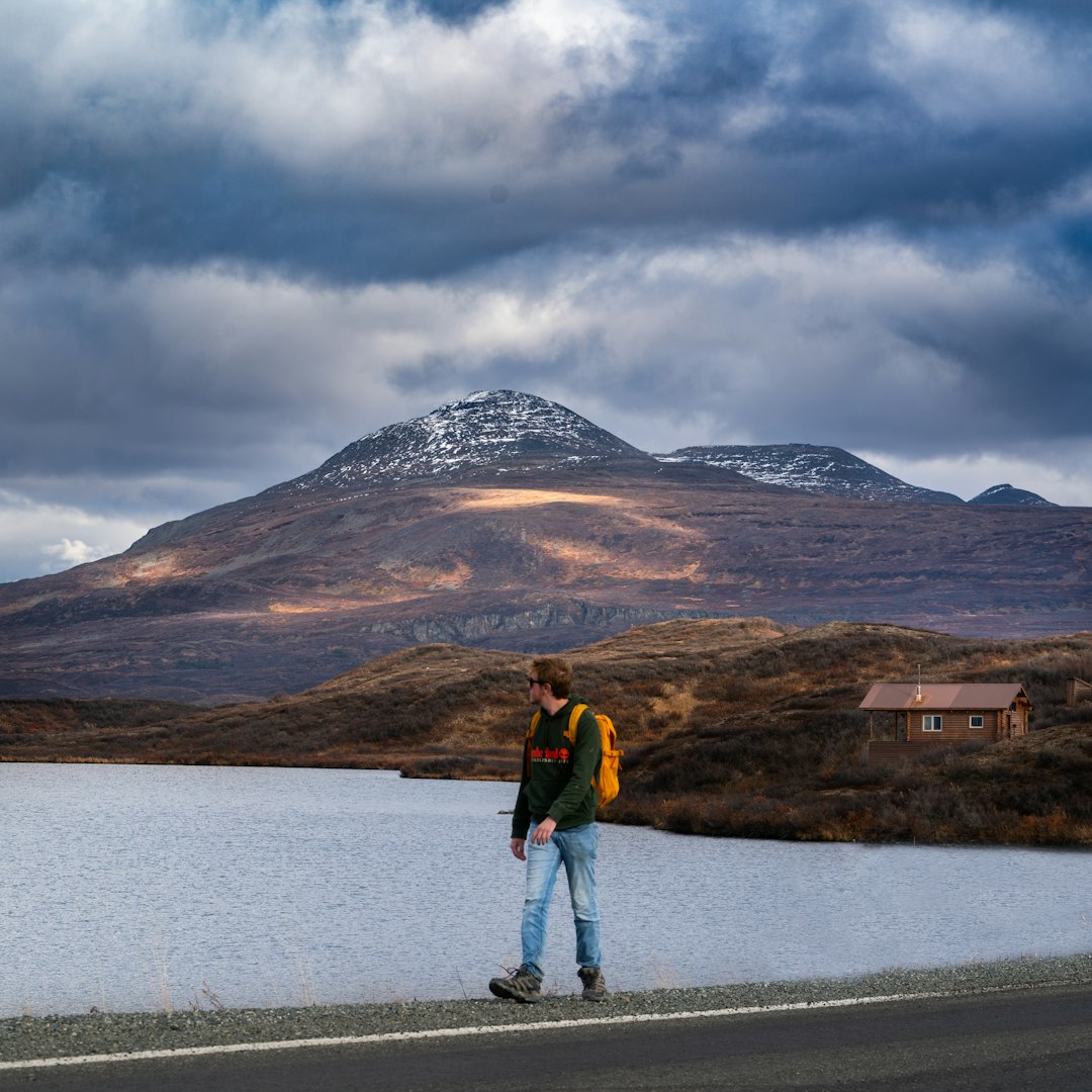 woman in red jacket walking on gray road near brown mountain under gray clouds during daytime