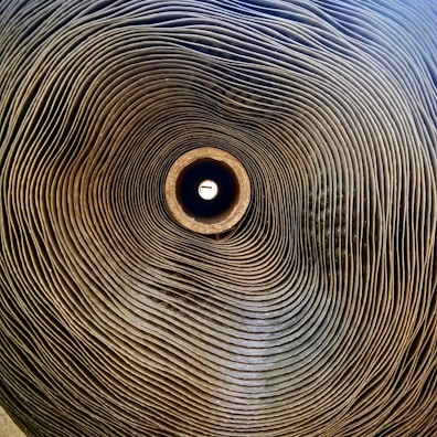 A tightly rolled stack of corrugated cardboard seen from a central perspective, creating a spiral pattern that draws the eye towards the bright center.