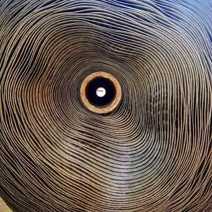 A tightly rolled stack of corrugated cardboard seen from a central perspective, creating a spiral pattern that draws the eye towards the bright center.