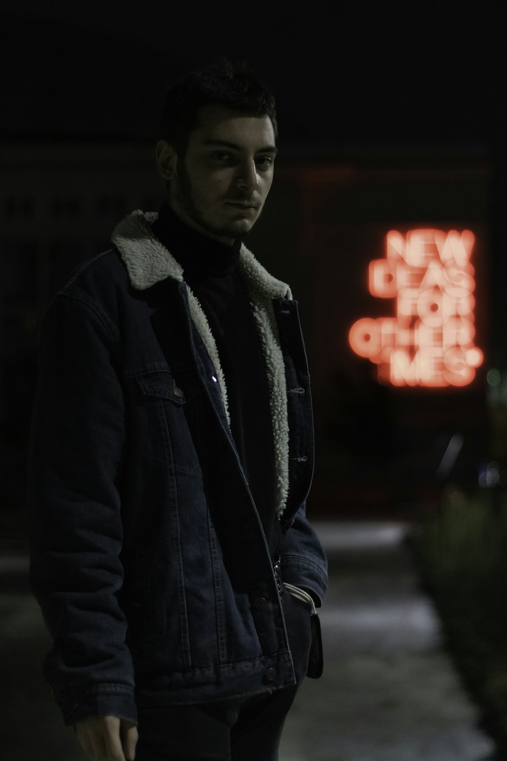 man in black jacket standing on sidewalk during night time