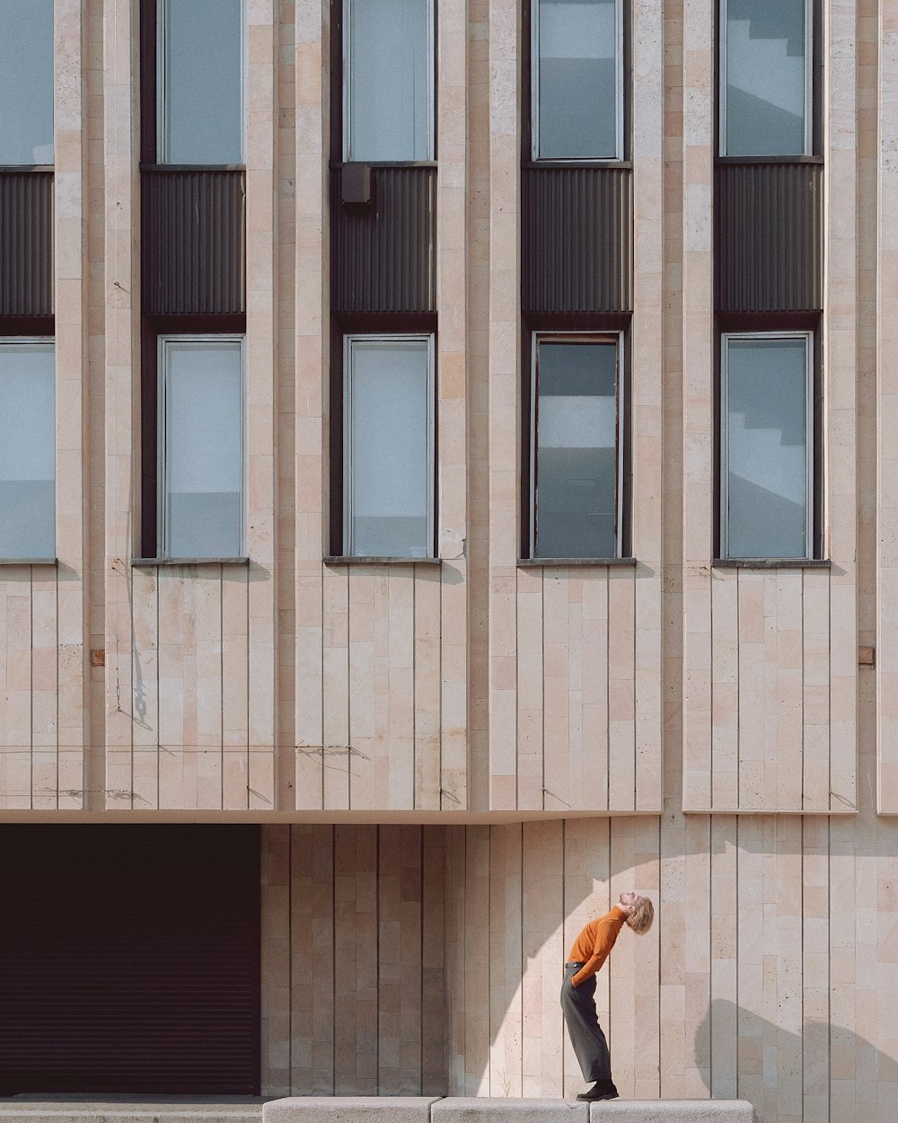 Person in orangefarbener Jacke vor braunem Gebäude