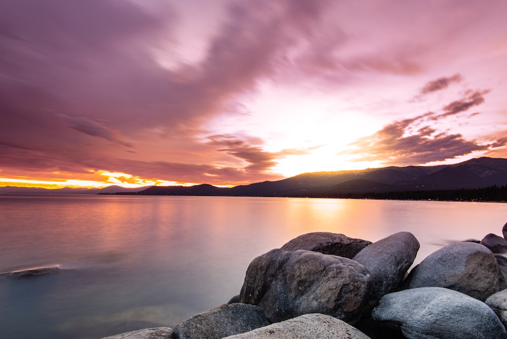 gray rocks near body of water during sunset