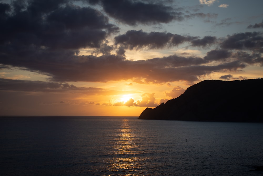 silhouette of mountain near body of water during sunset