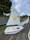 A row of small white sailboats is lined up on a textured surface with green grass nearby. Each boat has a sail, with the nearest one featuring a cheerful yellow star carrying a basketball and branding for Southern Cross Travel Insurance. The sailboat is labeled 'ATLAS CONCRETE' in red letters on its side.