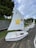 A row of small white sailboats is lined up on a textured surface with green grass nearby. Each boat has a sail, with the nearest one featuring a cheerful yellow star carrying a basketball and branding for Southern Cross Travel Insurance. The sailboat is labeled 'ATLAS CONCRETE' in red letters on its side.