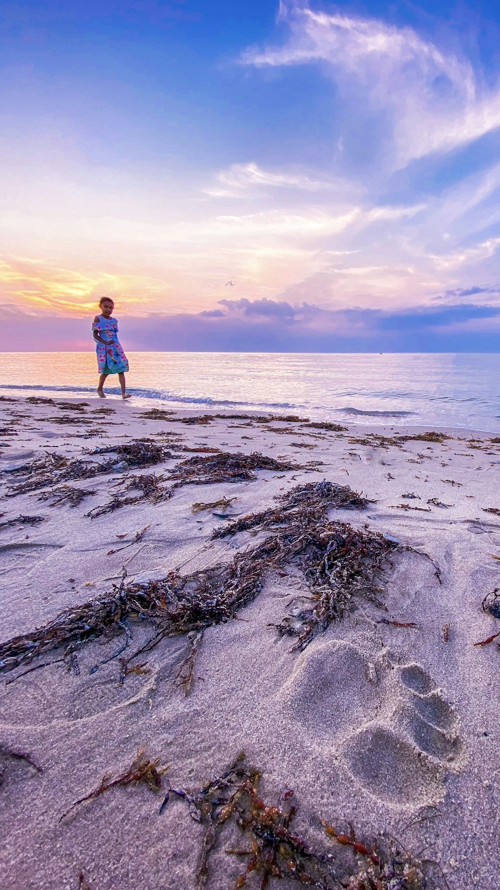 woman in red jacket and blue denim jeans standing on brown sand near body of water