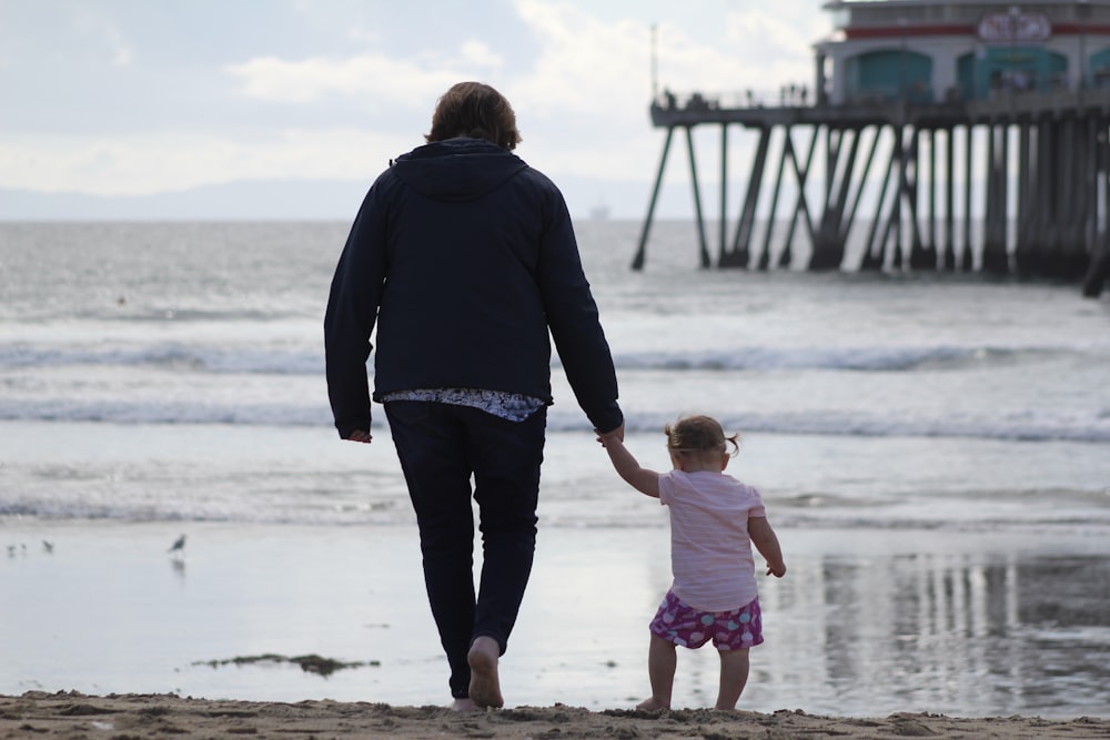 man in black jacket and girl in pink shirt walking on beach during daytime