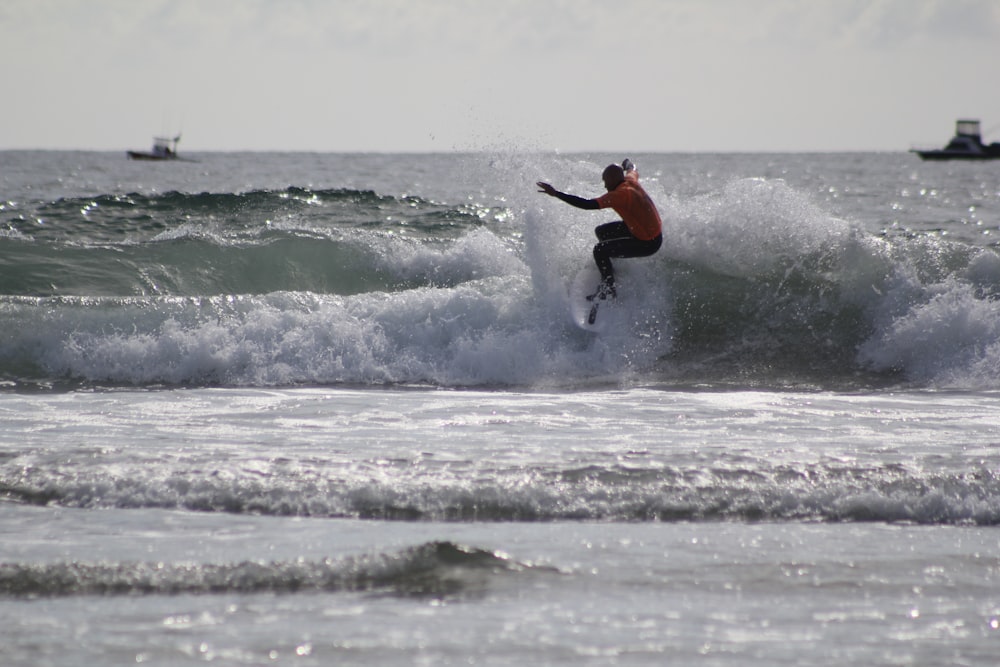 man in orange shirt surfing on sea waves during daytime