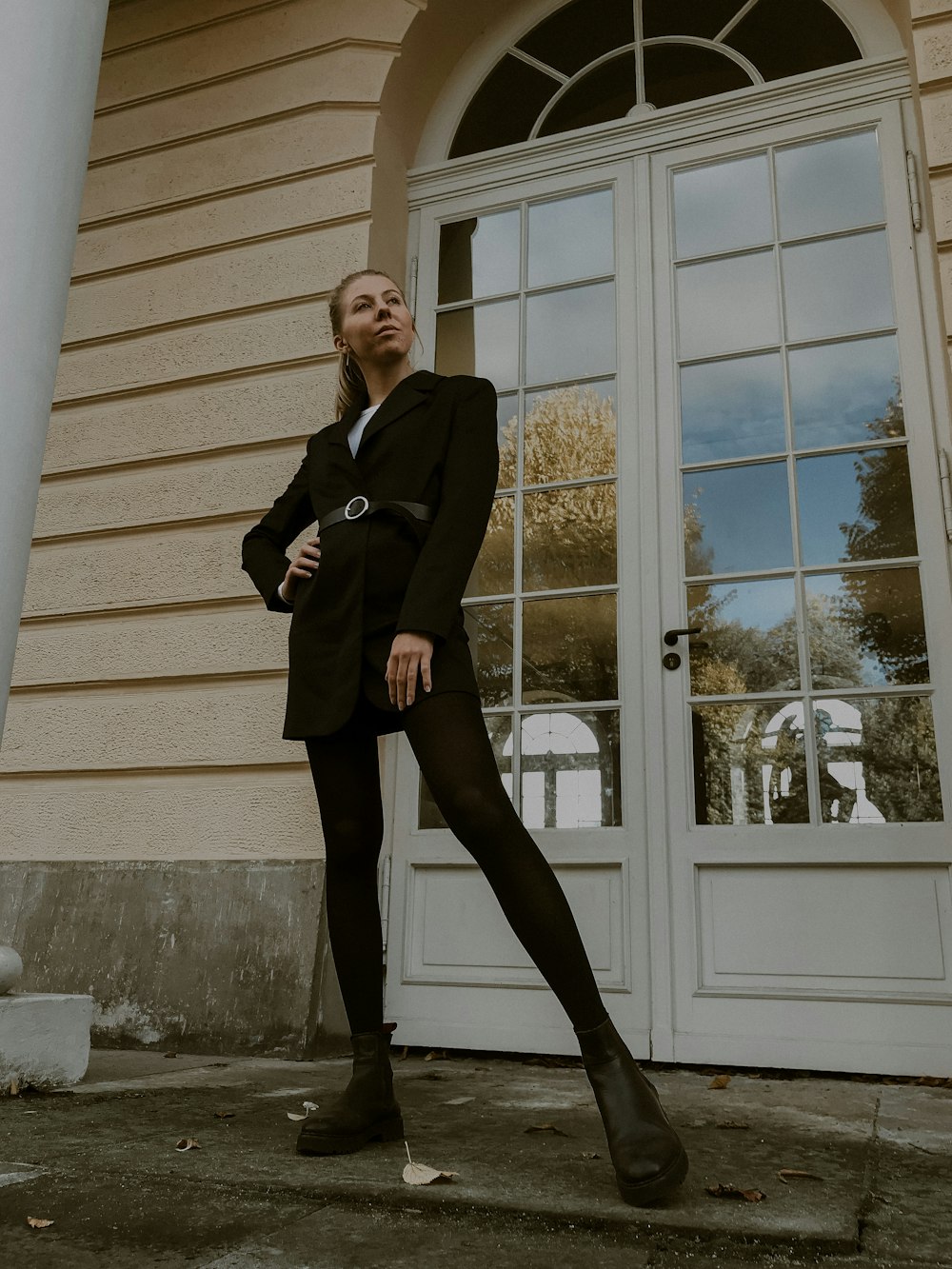 woman in black blazer and black dress pants standing beside white wooden framed glass window