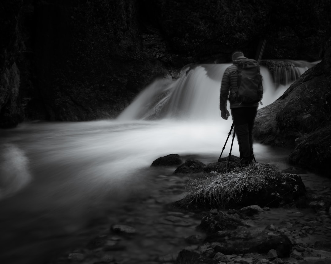 man in gray jacket standing on rock near waterfalls