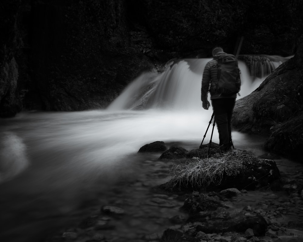 man in gray jacket standing on rock near waterfalls