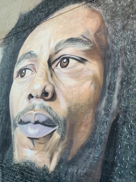 A detailed and realistic mural featuring the face of a man with dreadlocks and a contemplative expression. The artwork is rich in texture, capturing the intricate details of the hair and facial features.