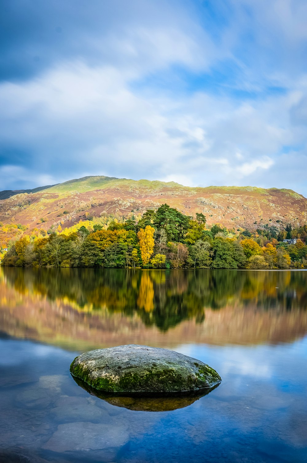 Grüner und brauner Berg am See tagsüber unter bewölktem Himmel