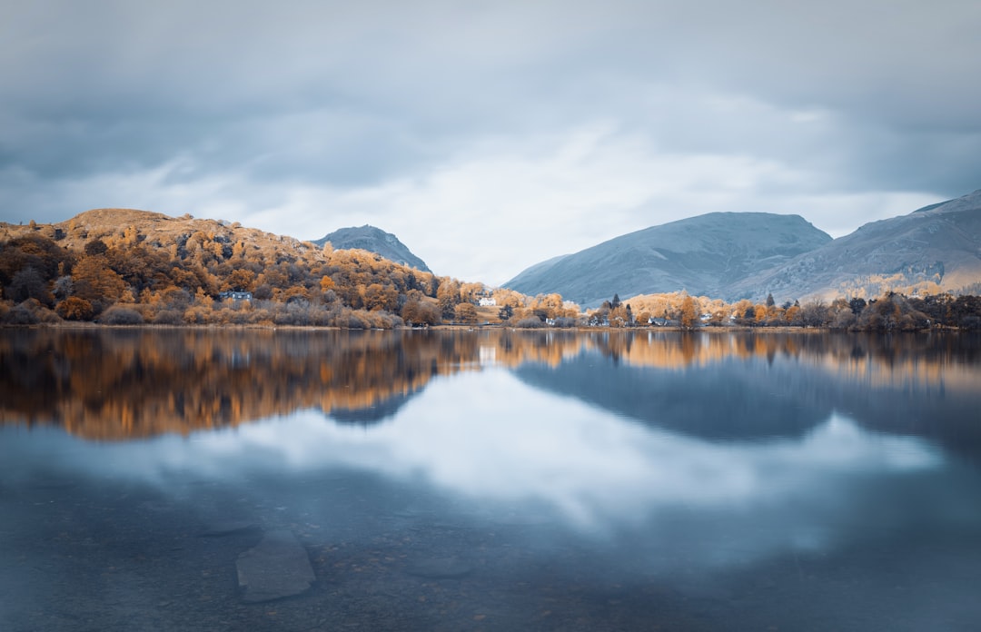 lake near mountain under white clouds during daytime