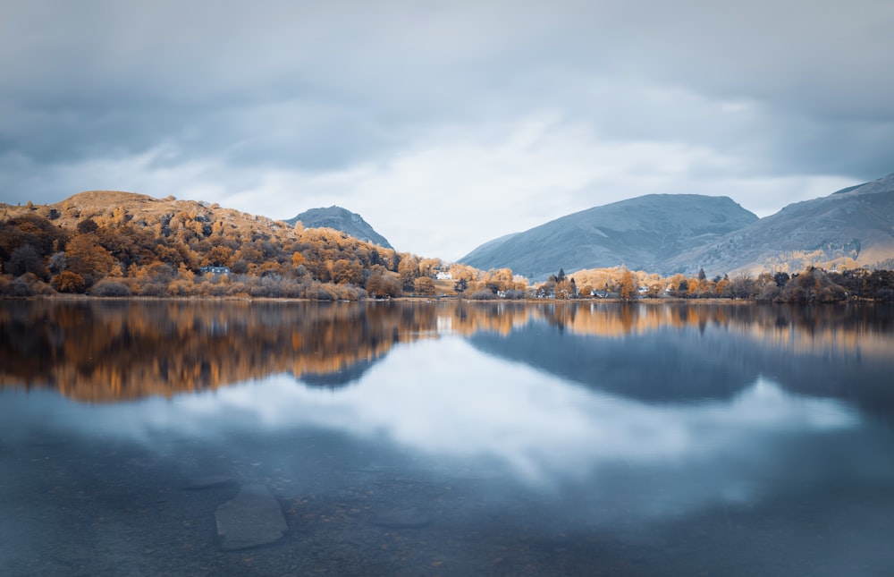 lake near mountain under white clouds during daytime