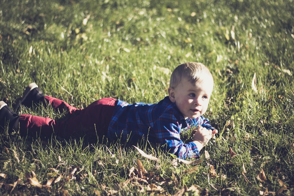 boy in blue and black jacket lying on green grass field during daytime
