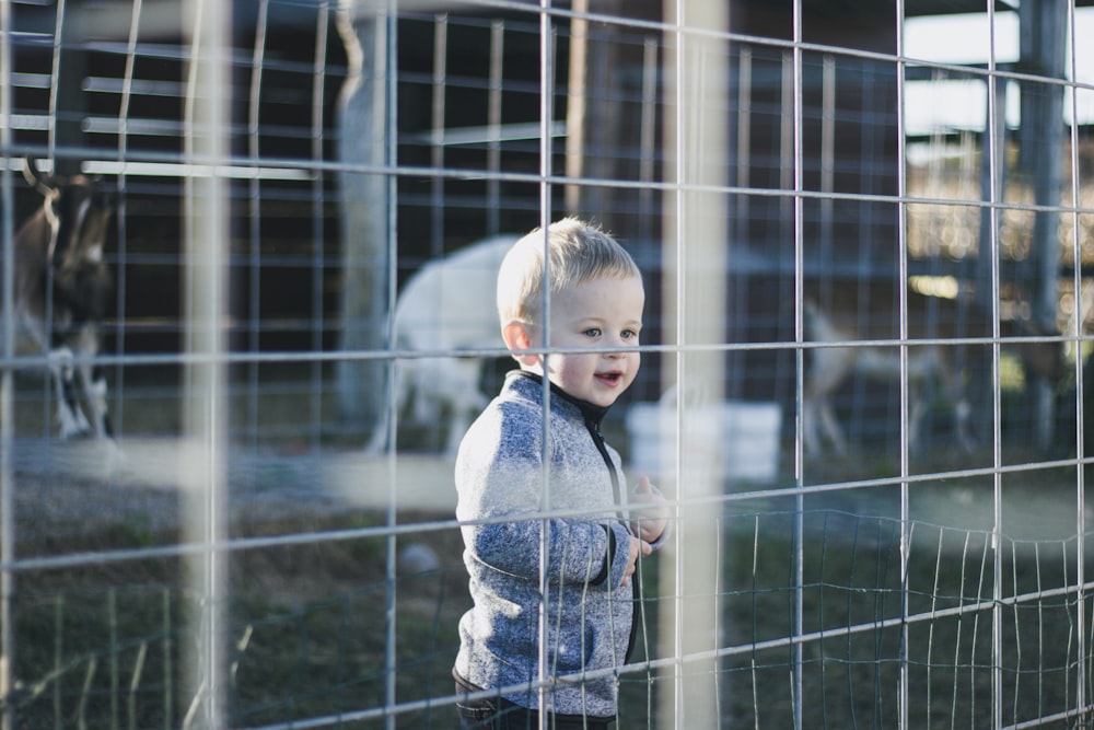 child in blue denim jacket standing near black metal fence during daytime