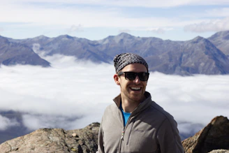 Close-up portrait of a smiling nomad with a rugged background of mountains and open sky.