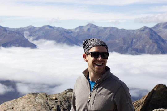 Close-up portrait of a smiling nomad with a rugged background of mountains and open sky.