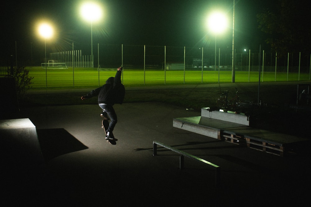 黒いジャケットとズボンを着た男が夜のフィールドでスケートボードをしている