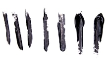 Six black brushstrokes of varying thickness and texture are arranged vertically on a white background. The strokes vary in smoothness and opacity, with some appearing more rough and textured while others are more glossy and solid.